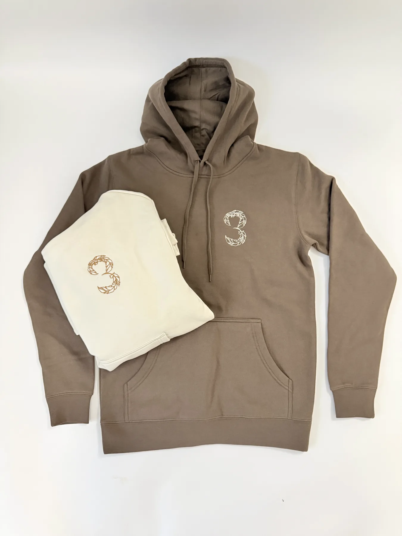 Brown and cream hoodies embroidered with the 3 Feathers mark