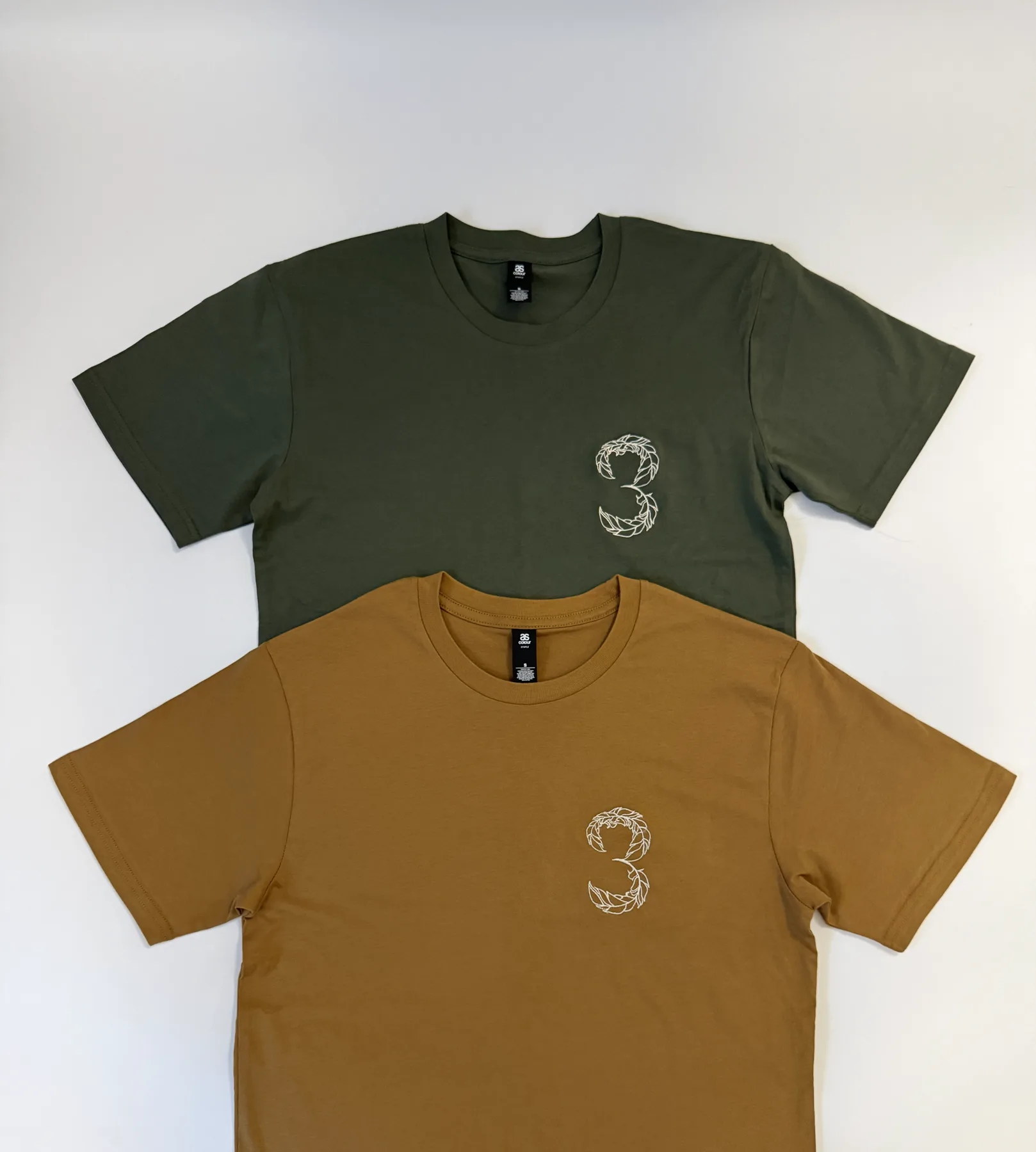 Green and gold T-shirts embroidered with the 3 Feathers mark